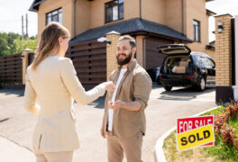 Realtor passing key to buyer Female realtor in suit passing house key to bearded man and congratulating him with buying cottage house
